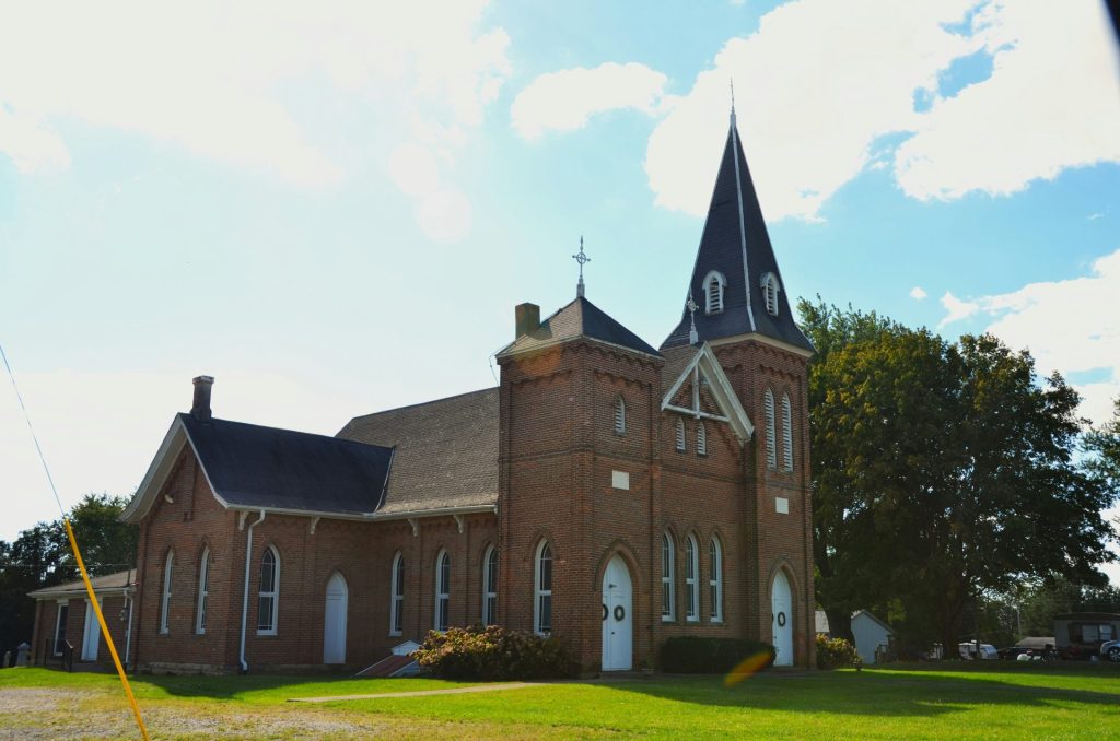 Brick church with a tall steeple on a sunny day.
